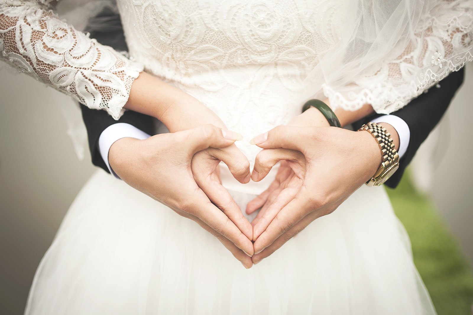 Bride and groom making a heart shape with their hands on her midriff