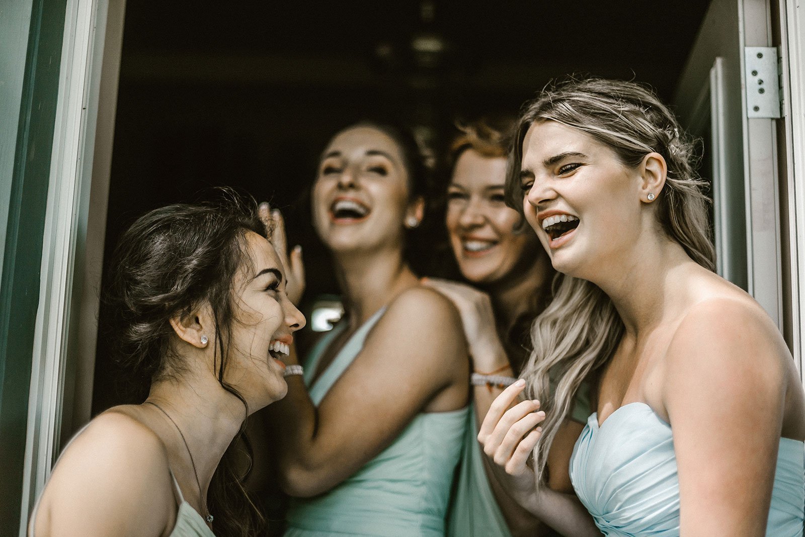 Group of bridesmaids standing in a doorway laughing wearing mint green dresses