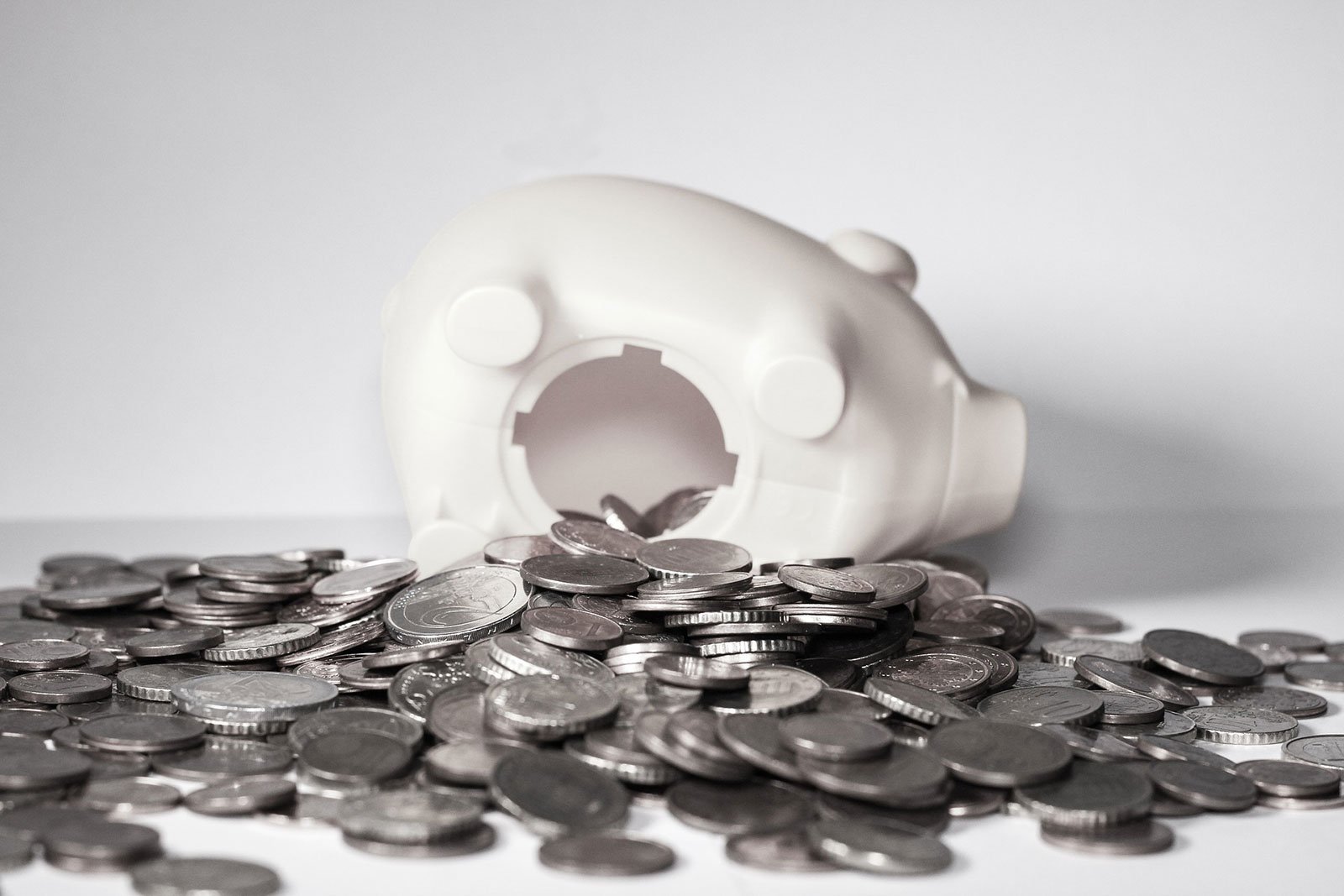 Coins scattered around white piggy bank that has fallen over