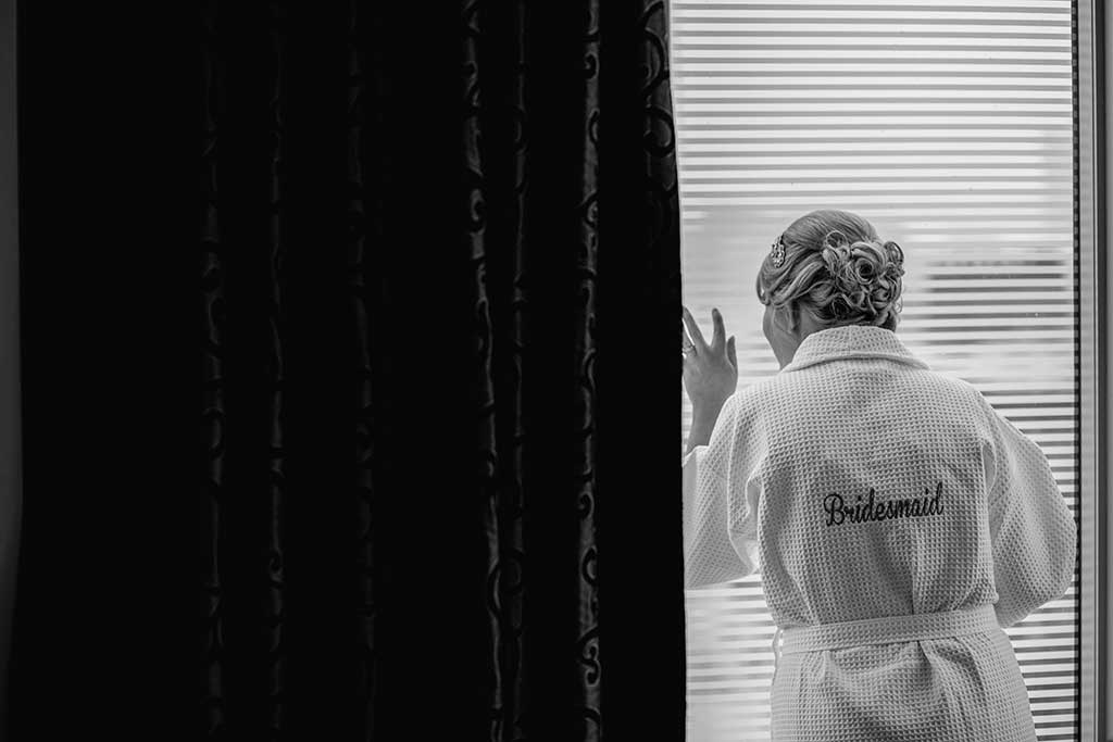 Girl in bridesmaid robe looking out the window in black and white